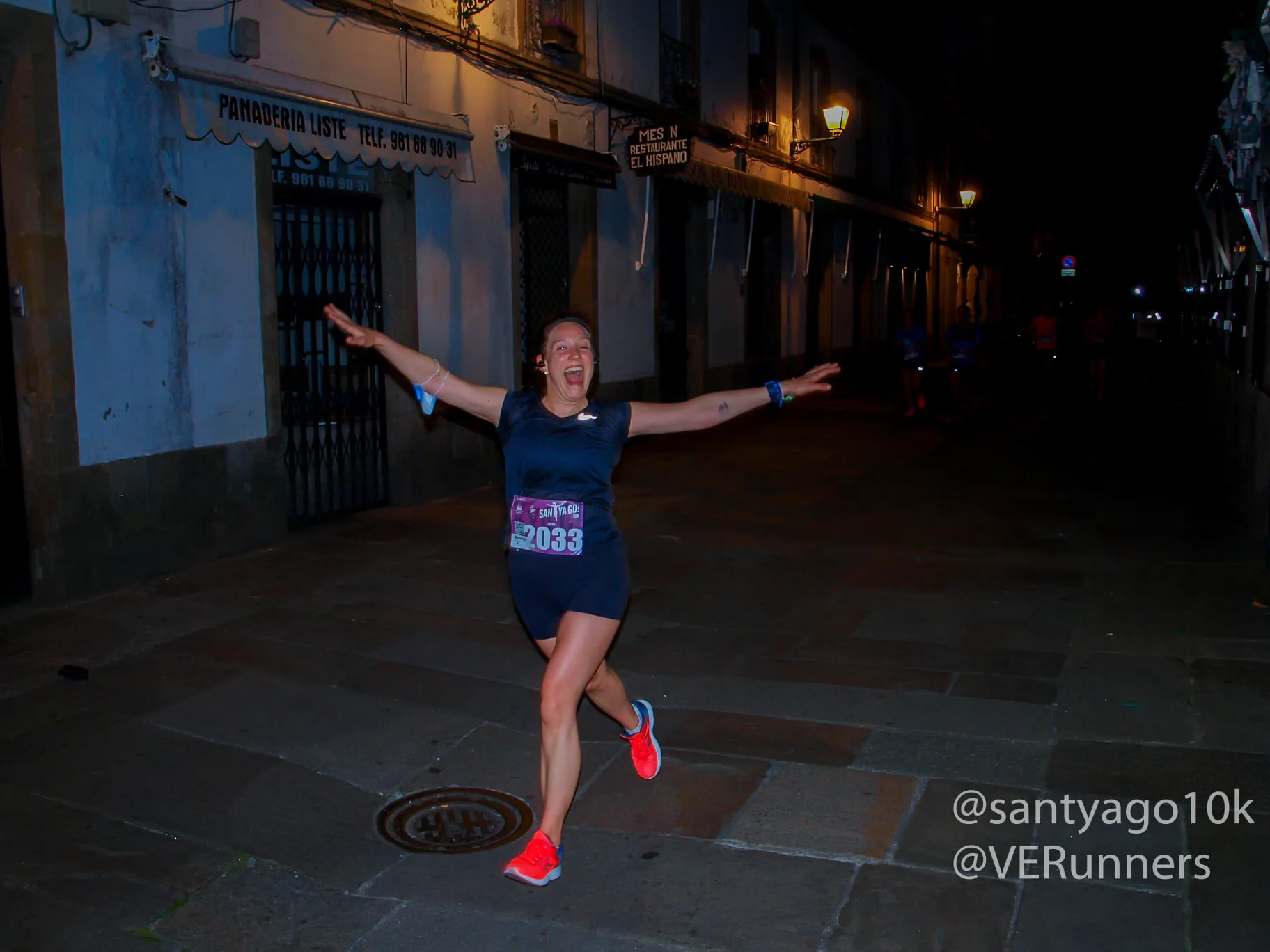 Joyful runner with arms spread wide celebrating while running through narrow historic streets at night